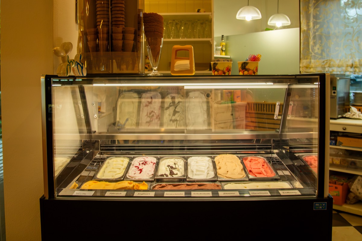 Eisvitrine mit vielen Sorten hausgemachtem Eis und gestapelten Waffelbechern