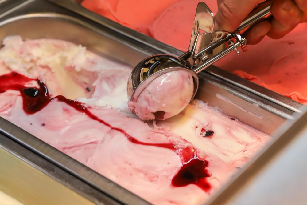 Eisportionierer schöpft eine Kugel Joghurt-Beeren-Eis aus der Wanne
