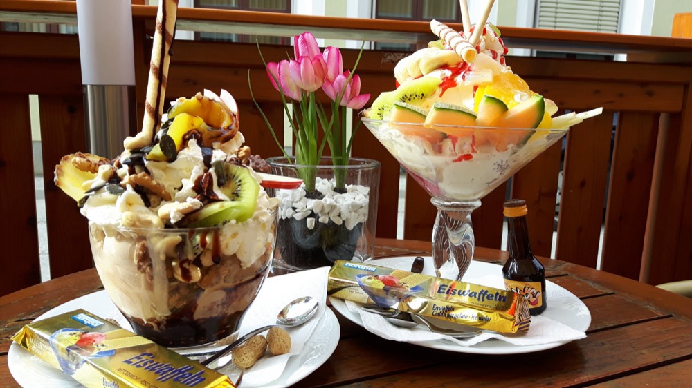 Zwei große Eisbecher mit Früchten, Nüssen und Waffelröllchen