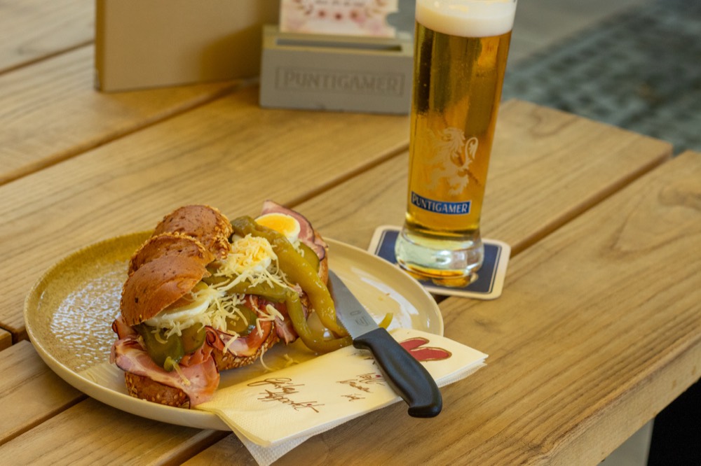 Belegtes Weckerl mit Ei und Pfefferoni neben einem Glas Bier auf dem Holztisch