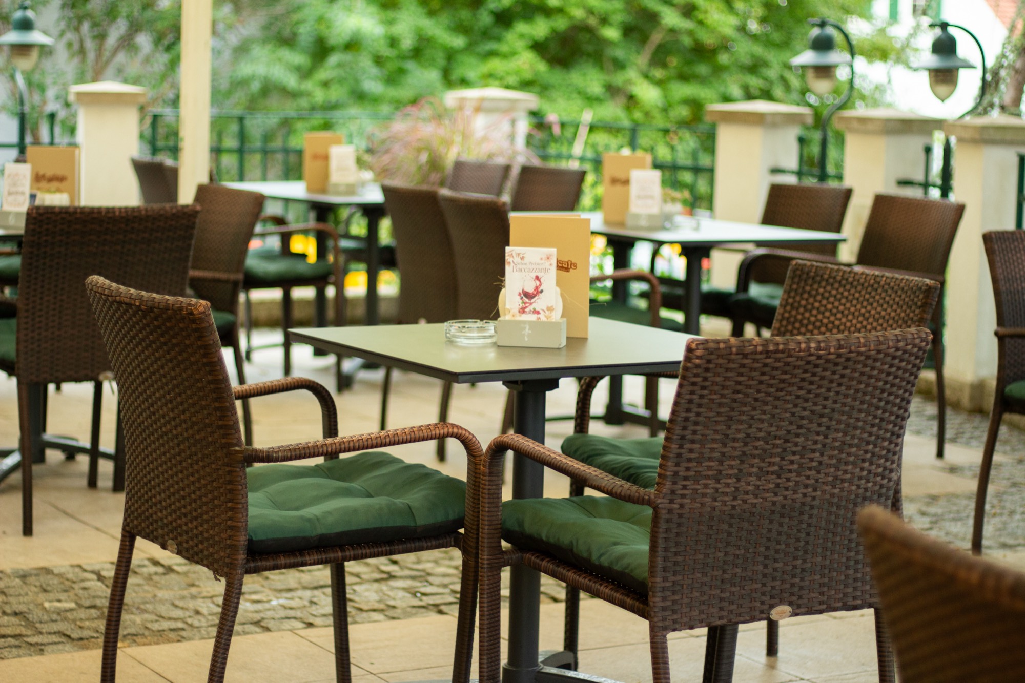 Gedeckte Tische im schattigen Gastgarten von Herwig´s Landcafe mit Korbstühlen und grünen Sitzkissen
